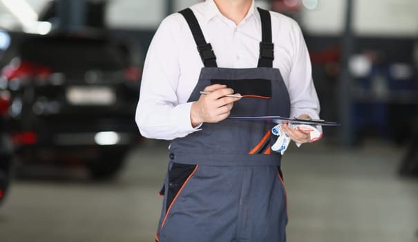 Auto mechanic holding clipboard and pen in car service. Service and repair auto concept