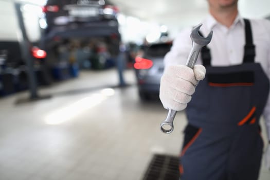 Car repairman in uniform holds wrench in car workshop. Car service concept and auto service