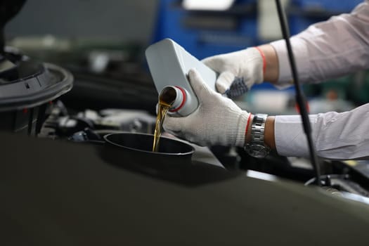 Closeup of experienced mechanic checking and pouring oil into special hole in car. Changing oil in car engine concept