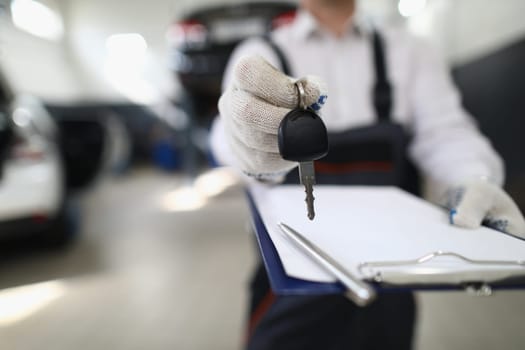 Auto mechanic holds clipboard and car keys. Car warranty repair services.Checking order for maintenance of vehicles working in garage