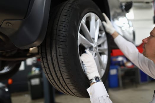 Auto mechanic in car repair shop inspects the wheels and suspension of car on lift. Auto repair shop and car maintenance