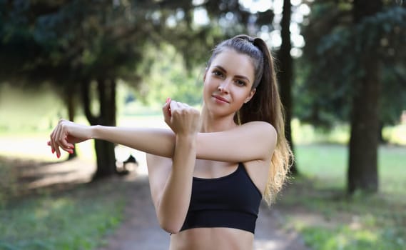 Portrait of beautiful sports woman stretches arms in park. Morning exercise outdoors concept