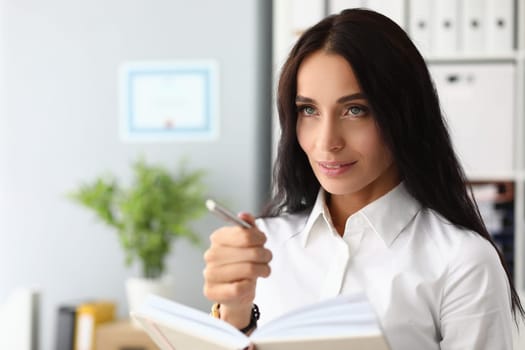 Portrait of a pensive beautiful businesswoman with pen and diary. Working time planning and day concept