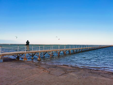 Bridge on the ocean coast. Man stands and looks at the paraglider. Sea coast on a quiet day