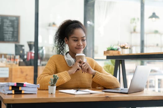 Beautiful American women student studying online takes notes on her laptop to gather information about her work smiling face and a happy study posture..