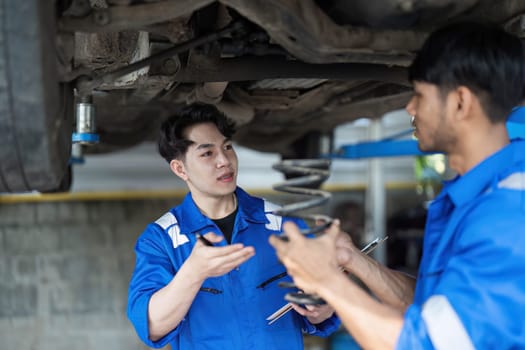 Two Mechanics in a Service are Inspecting a Car After They Got the Diagnostics Results. Female Specialist is Comparing the Data on a Tablet Computer. Repairman is Using a Ratchet to Repair the Faults...