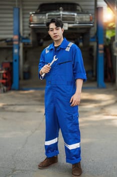 Portrait Shot of a Handsome Mechanic Working on a Vehicle in a Car Service. Professional Repairman is Wearing Gloves and Using a Ratchet Underneath the Car. Modern Clean Workshop...