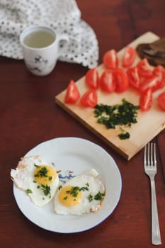 fried eggs, cherry-tomatoes with cup on dark table surface, top view.