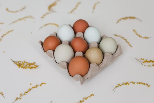 fresh chicken eggs of natural shades and colors in a recycled box on a white background.