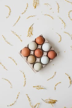fresh chicken eggs of natural shades and colors in a recycled box on a white background.