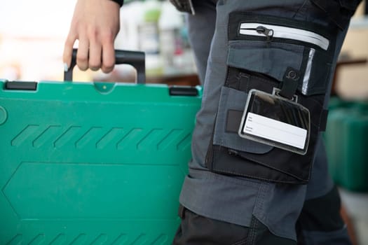 A close-up view of a woman dressed in work clothes holding a plastic green tool case.