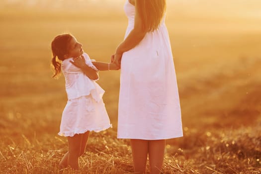 Positive little girl with her mother have weekend outdoors on the summer field together.