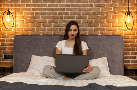 Happy beautiful woman is sitting on the bed and working on the laptop.