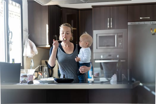Happy mother and little infant baby boy prepering healthy breakfast together in domestic kitchen. Family, lifestyle, domestic life, food, healthy eating and people concept