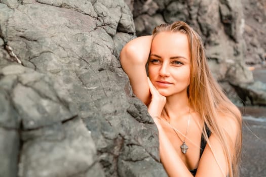 Woman swimsuit sea. Attractive blonde woman in a black swimsuit enjoying the sea air on the seashore around the rocks. Travel and vacation concept