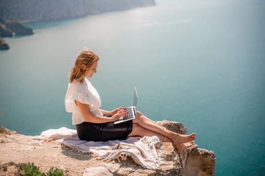 Freelance women sea working on the computer. Good looking middle aged woman typing on a laptop keyboard outdoors with a beautiful sea view. The concept of remote work