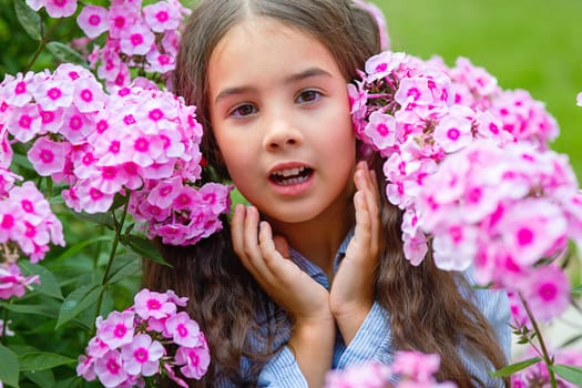 Portrait of adorable little girl in lush pink phlox flowers, summer. Close up