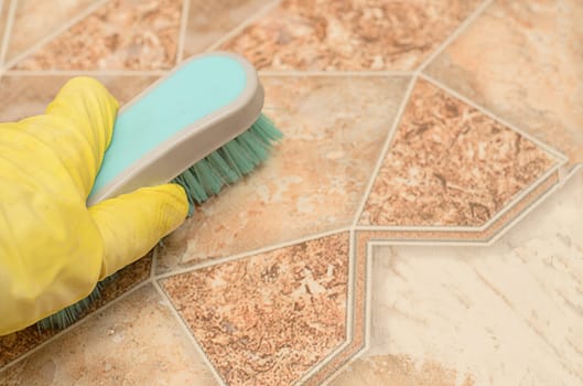 Man in yellow glove holds a brush for cleaning kitchen floor.