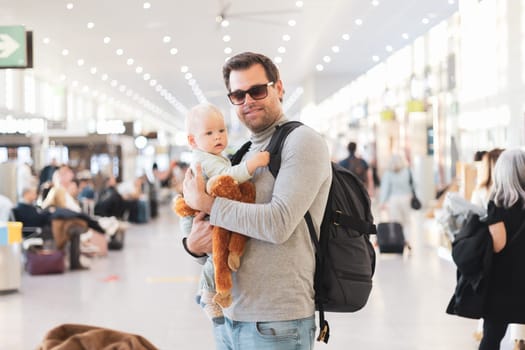 Father traveling with child, holding his infant baby boy at airport terminal waiting to board a plane. Travel with kids concept