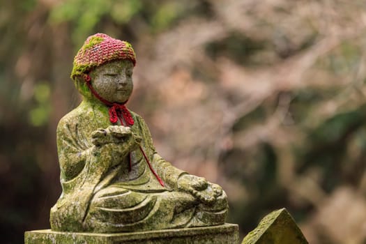 Stone statue of child sitting peacefully at Japanese buddhist temple in forest. High quality photo