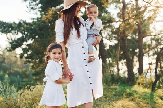 Young mother with her little daughter and son is outdoors in the forest. Beautiful sunshine.