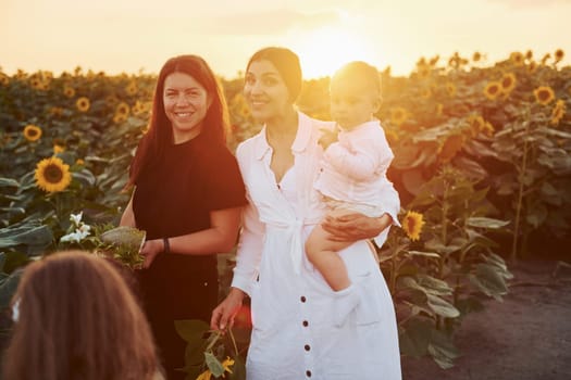 Young mother with her little son, daughter and female friend is outdoors in the agricultural field. Beautiful sunshine.
