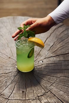 Waiter's hand. With lemon and mint. Close up view of fresh summer alcoholic cocktail on the wooden table.