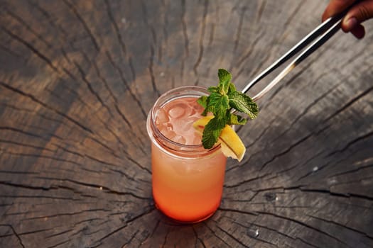 Waiter's hand. With lemon and mint. Close up view of fresh summer alcoholic cocktail on the wooden table.