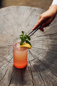 Waiter's hand. With lemon and mint. Close up view of fresh summer alcoholic cocktail on the wooden table.