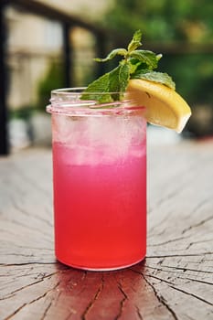 Pink colored liquid with lemon. Close up view of fresh summer alcoholic cocktail on the wooden table.