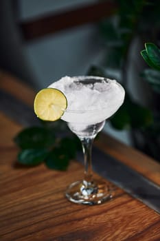 Piece of lime on top. Close up view of fresh summer cocktail on the wooden table.