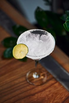 Piece of lime on top. Close up view of fresh summer cocktail on the wooden table.