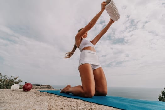 Woman sea pilates. Sporty, middle-aged woman practicing pilates in park near the sea. trains on a yoga mat and exudes a happy and active demeanor, promoting the idea of a healthy lifestyle through exercise and meditation.