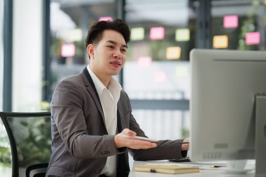 Smiling Asian Banker makes financial report and studies annual figures, analyzes profits. Accountant checks status of financial.