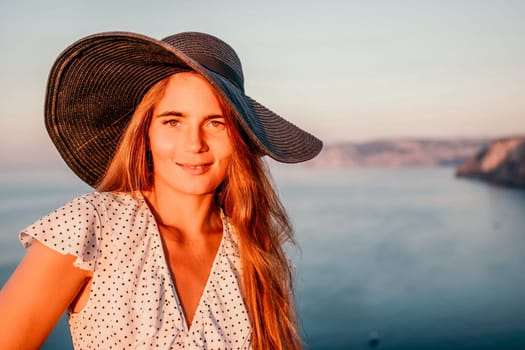 Portrait of happy young woman wearing summer black hat with large brim at beach on sunset. Closeup face of attractive girl with black straw hat. Happy young woman smiling and looking at camera at sea