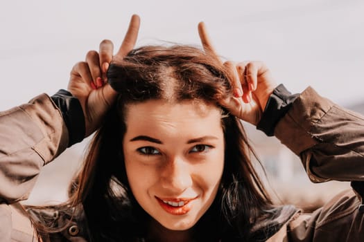 Happy young smiling woman with freckles outdoors portrait. Soft sunny colors. Outdoor close-up portrait of a young brunette woman and looking to the camera, posing against nature background.