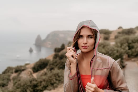 Woman rain park. Happy woman portrait wearing a raincoat with transparent umbrella outdoors on rainy day in park near sea. Girl on the nature on rainy overcast day