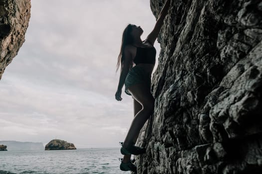 A girl climbs a rock. The athlete trains in nature. Woman overcomes difficult climbing route. Extreme hobby. Tourist woman rock climber hiking on mountains rocks over beautiful sea coast