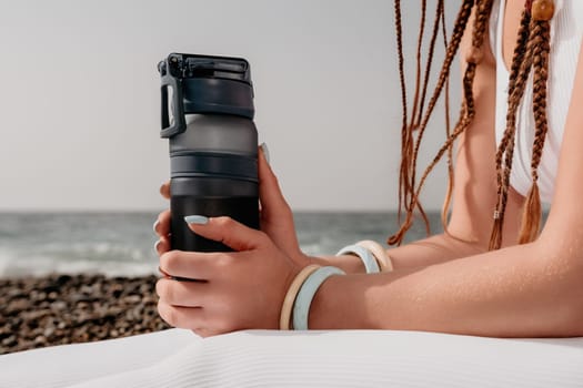 Woman yoga sea. Well looking middle aged woman with braids dreadlocks in white leggings and tops doing stretching pilates on yoga mat near sea. Female fitness yoga routine concept. Healthy lifestyle