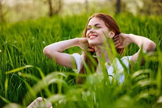 beautiful, elegant woman with red hair sits in tall green grass and smiles. High quality photo