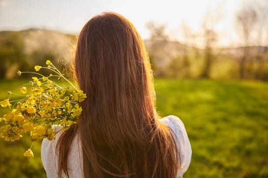 photo from the back of a red-haired woman with a bouquet of flowers in the rays of the setting sun. High quality photo
