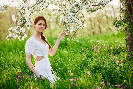 Beautiful woman in a blooming spring garden in a light dress smiling looking at the camera. High quality photo