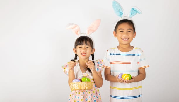 Happy Easter Day. Two smile Asian little girl and boy wearing easter bunny ears holding basket with eggs isolated on white background with copy space, Happy family children in holiday