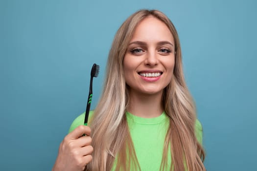 young blond woman with healthy teeth holding a toothbrush on a blue background.