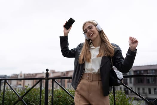 photo of a young woman blogger listening to a podcast in headphones on the street.
