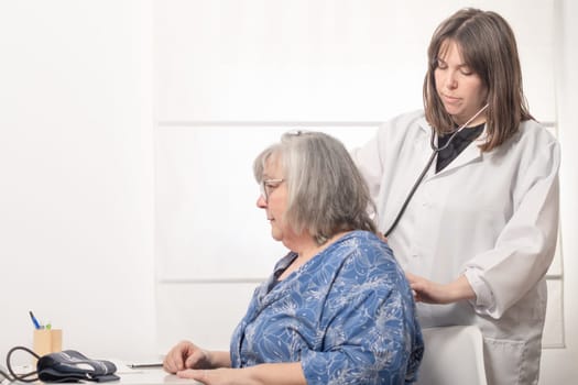 young female doctor auscultating her patient's back with a stethoscope in the doctor's office