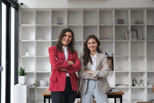 Two successful businesspeople in formal wear standing in modern office and looking confidently at camera..