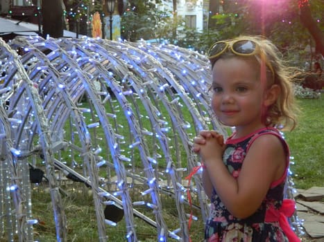 A little girl is standing in front of a sculpture that has lights on it. High quality photo