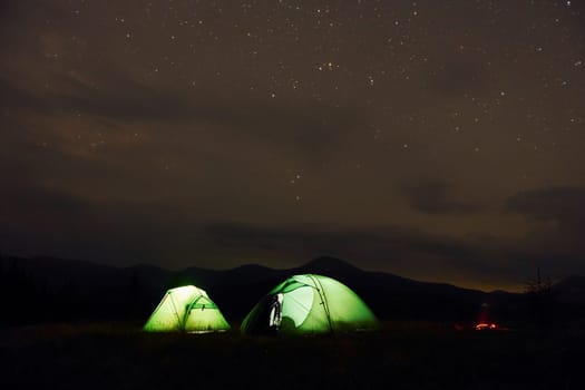 Green tents at night time. Starry sky. Majestic Carpathian Mountains. Beautiful landscape of untouched nature.