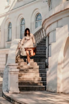 Woman walks in the city, lifestyle. Young beautiful woman in a loose light sweater, brown skirt and sneakers with a hat